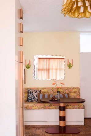 Zona de menjador amb taula rodona, seients de banc i finestra decorativa amb cortines.