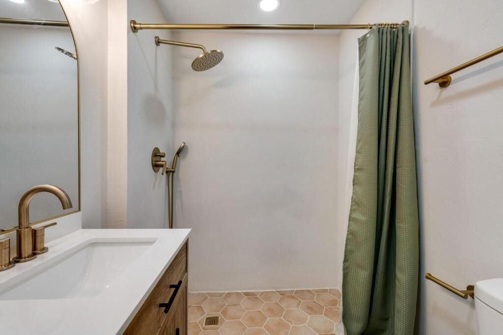 A bathroom with a white sink, gold fixtures, a shower with a green curtain, and a hexagonal tile floor.