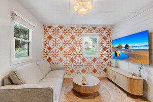 A modern living room with a sofa, a round coffee table, a TV mounted on the wall, and a patterned wallpaper.