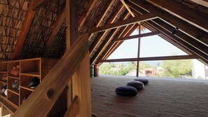 A room with a sloped ceiling, wooden beams, a large window, and a carpeted floor. - luxury 6-bdr building in gorgeous Brisas de Zicatela with AC, pool and yoga area (Brisas de Zicatela)