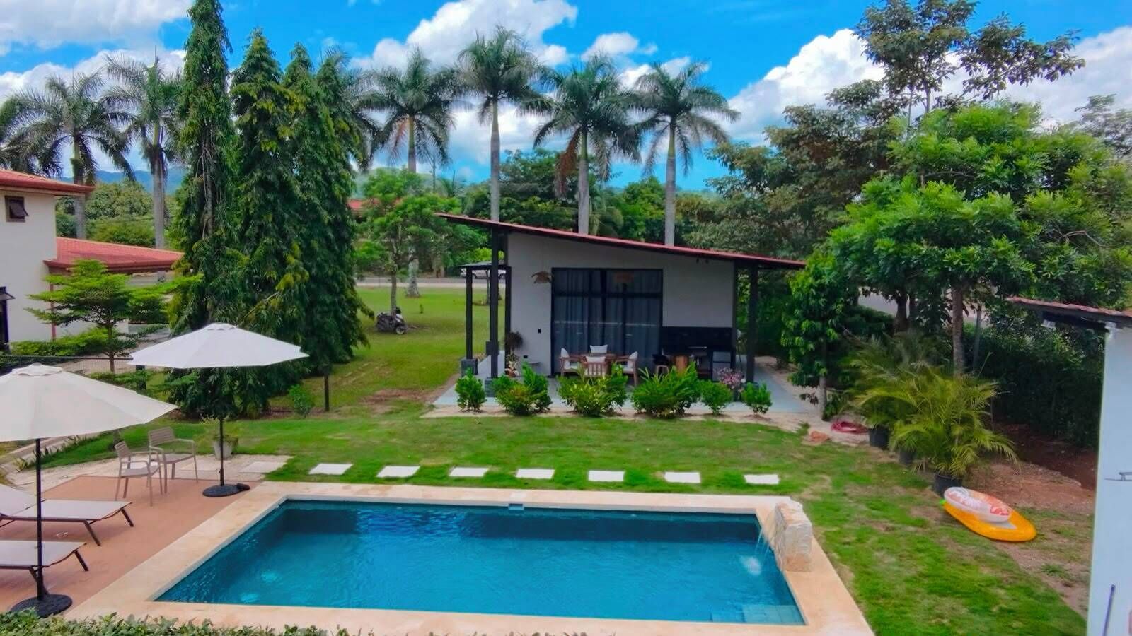 A swimming pool with a patio area, surrounded by lush greenery and palm trees.