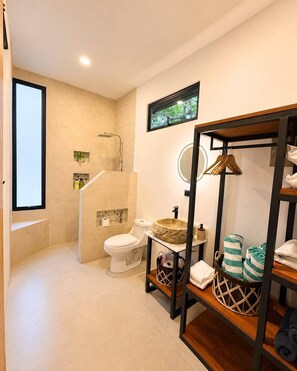 A modern bathroom with a shower, toilet, and sink. There is a wooden shelf with towels and a basket.