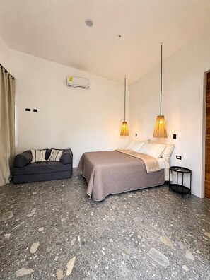 A bedroom with a bed, a sofa, a small table, an air conditioning unit, and pendant lights.