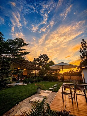 A patio area with a wooden deck, outdoor furniture, and a view of the sunset.