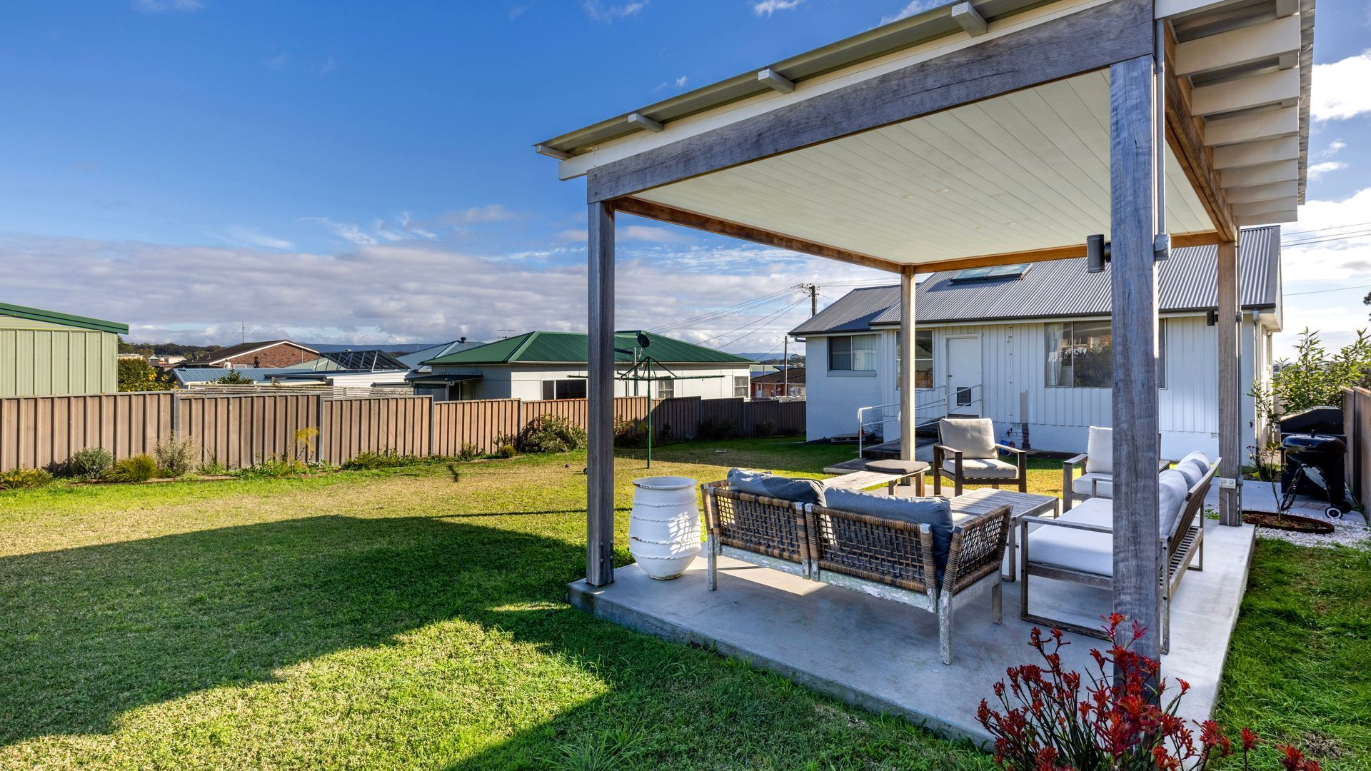 A covered patio area with outdoor furniture, a barbecue grill, and a fenced backyard.