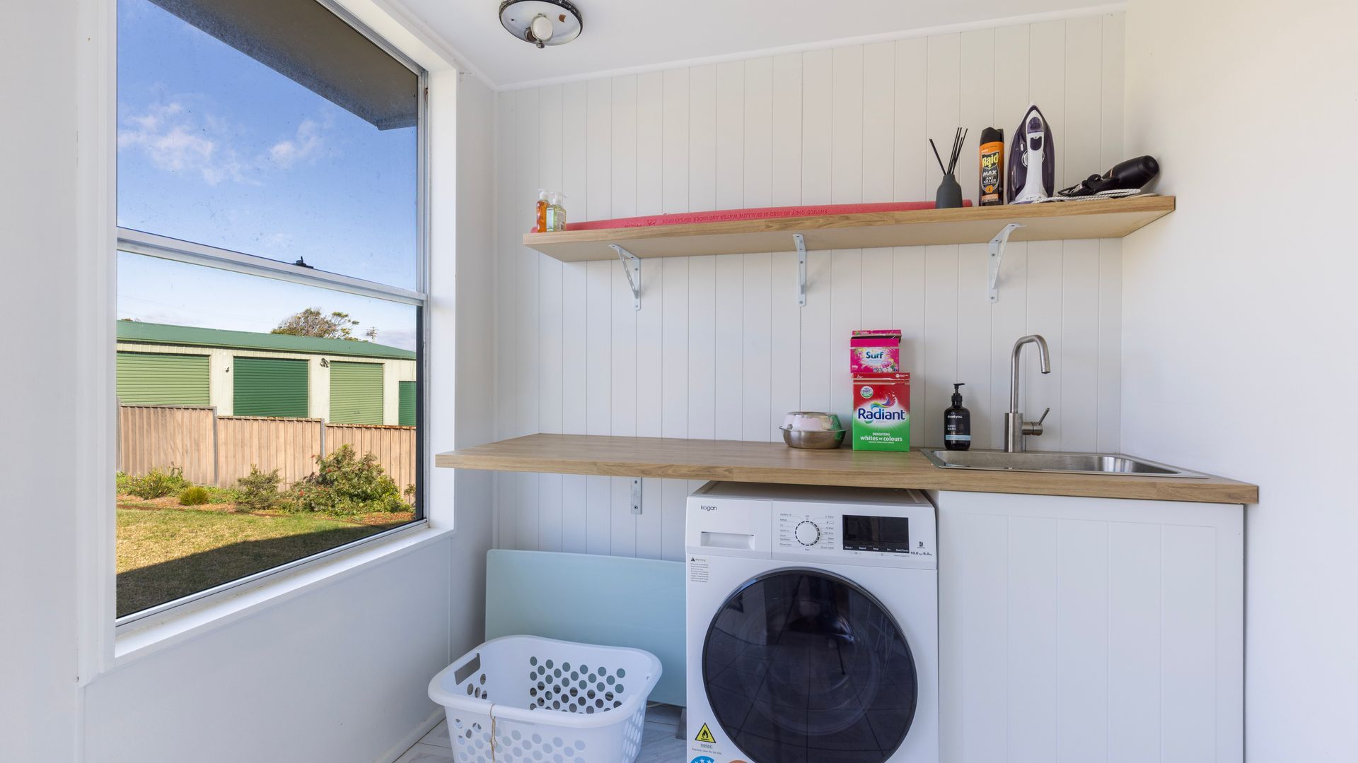 A laundry area with a washing machine, a sink, and storage shelves.