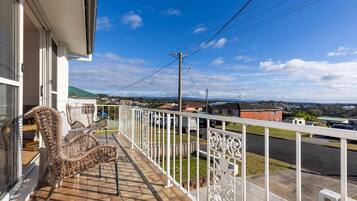 Un balcon avec des fauteuils en osier, une balustrade blanche et une vue sur un quartier résidentiel avec des maisons et une rue.