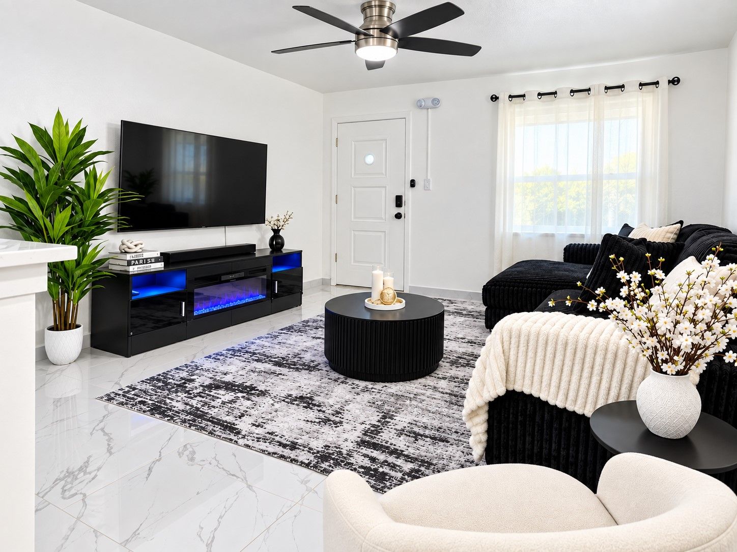 A modern living room with a flat-screen TV, black entertainment unit, round coffee table, and a black and white patterned rug.