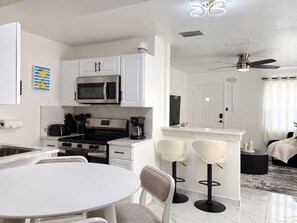 A modern kitchen with white cabinets, a stainless steel stove, and a microwave. There is a dining area with a white table and chairs. - 🌴🍹Cozy Retreat 3BR Near Tampa, Disney, Legoland (Lakeland)