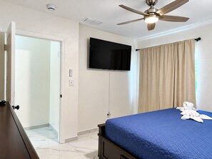 A hotel room with a bed, a ceiling fan, a television mounted on the wall, and a door leading to another room. - 🌴🍹Cozy Retreat 3BR Near Tampa, Disney, Legoland (Lakeland)