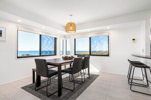Ein Essbereich mit Tisch und Stühlen, große Fenster mit Meerblick und einer hängenden Leuchte.