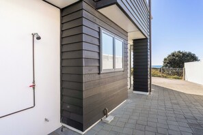 A building with a dark siding exterior, a visible window, and a paved patio area. - Sunbrae Sands - Mount Maunganui Holiday Homes (Mount Maunganui)