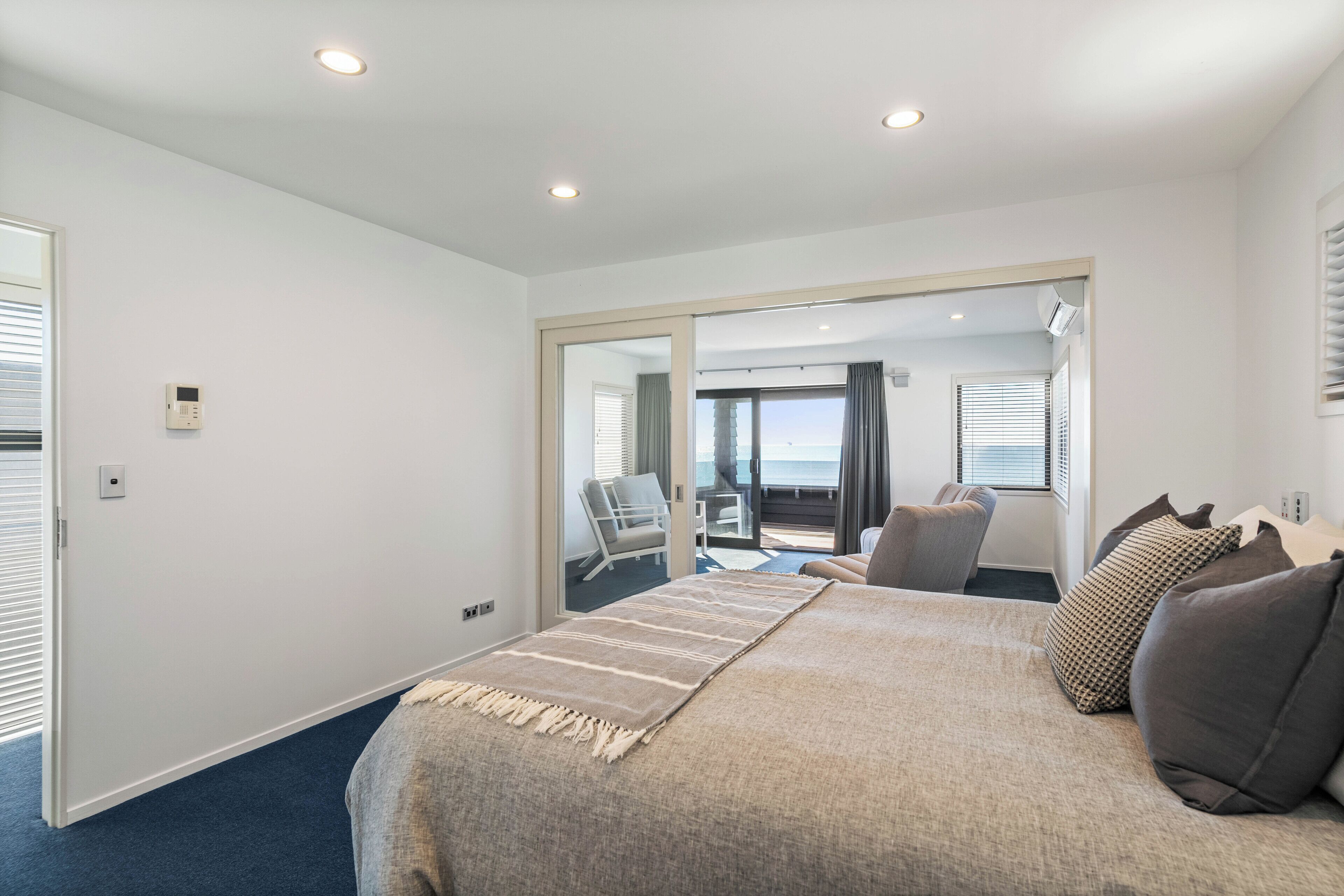 Ein Schlafzimmer mit Bett, Sessel, einem Balkon mit Blick und einer Tür zu einem weiteren Raum.