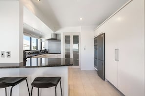 A modern kitchen with a central island, stainless steel appliances, and a view to the outside. - Sunbrae Sands - Mount Maunganui Holiday Homes (Mount Maunganui)