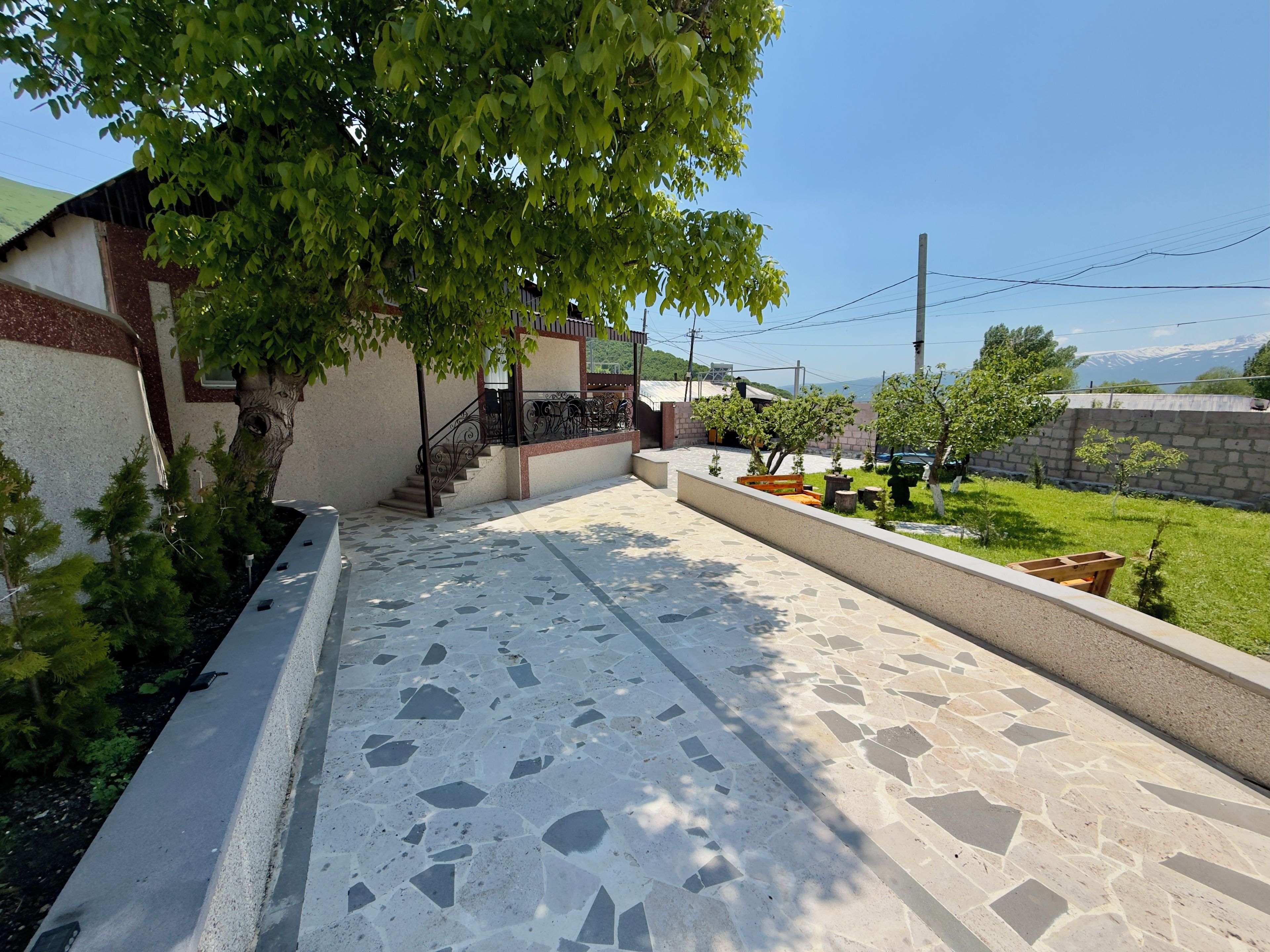 A courtyard with a tiled floor, a staircase, and a tree providing shade.