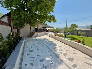Pátio com piso de azulejos, escadaria e árvore que oferece sombra.