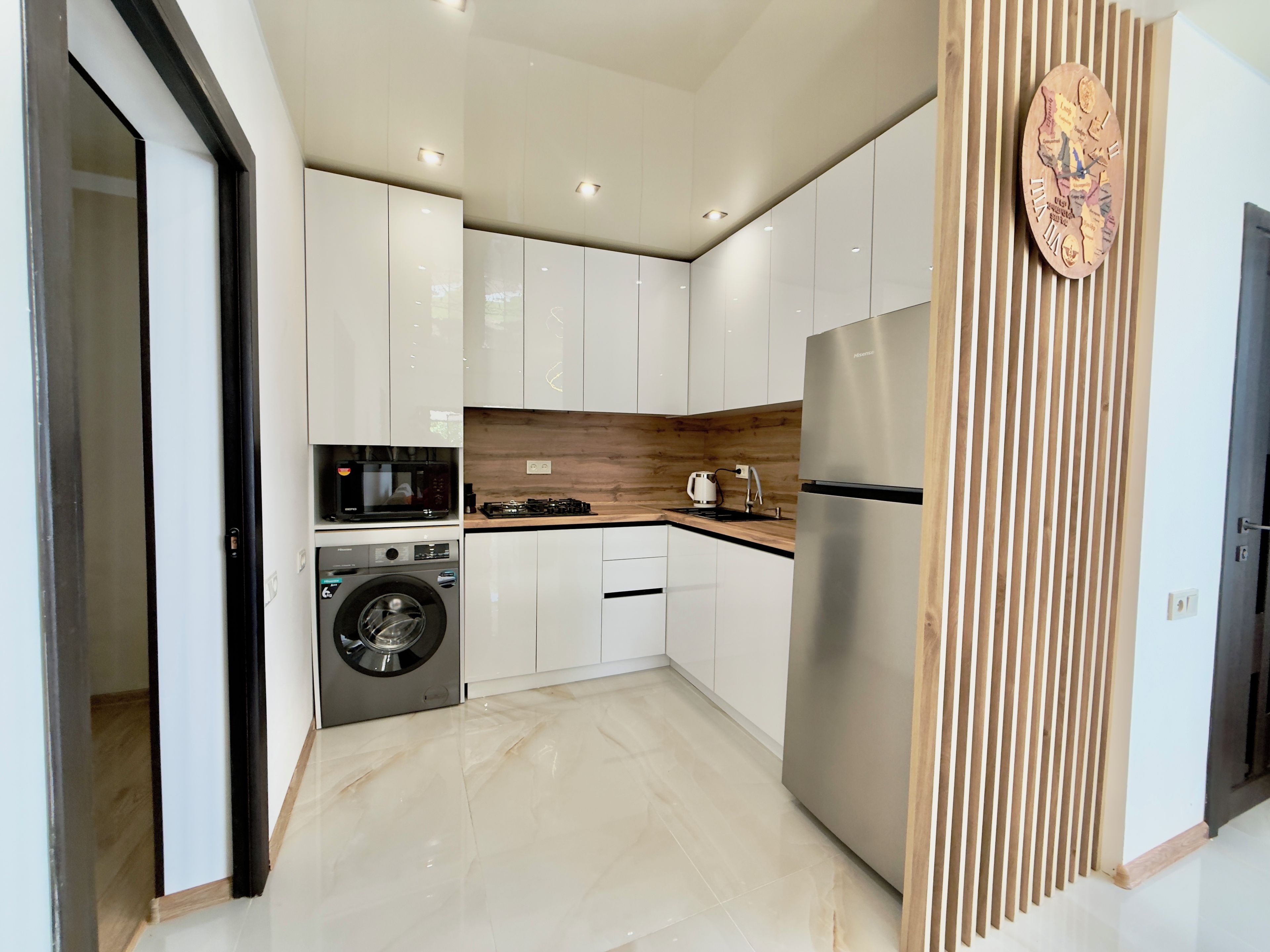 Eine moderne Küche mit weißen Schränken, einem Edelstahl-Kühlschrank, einer Waschmaschine und einer Mikrowelle.