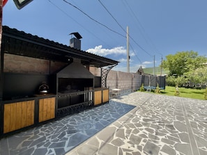 Uma área de cozinha externa com piso de pedra, parede de tijolo e estrutura de telhado em metal.