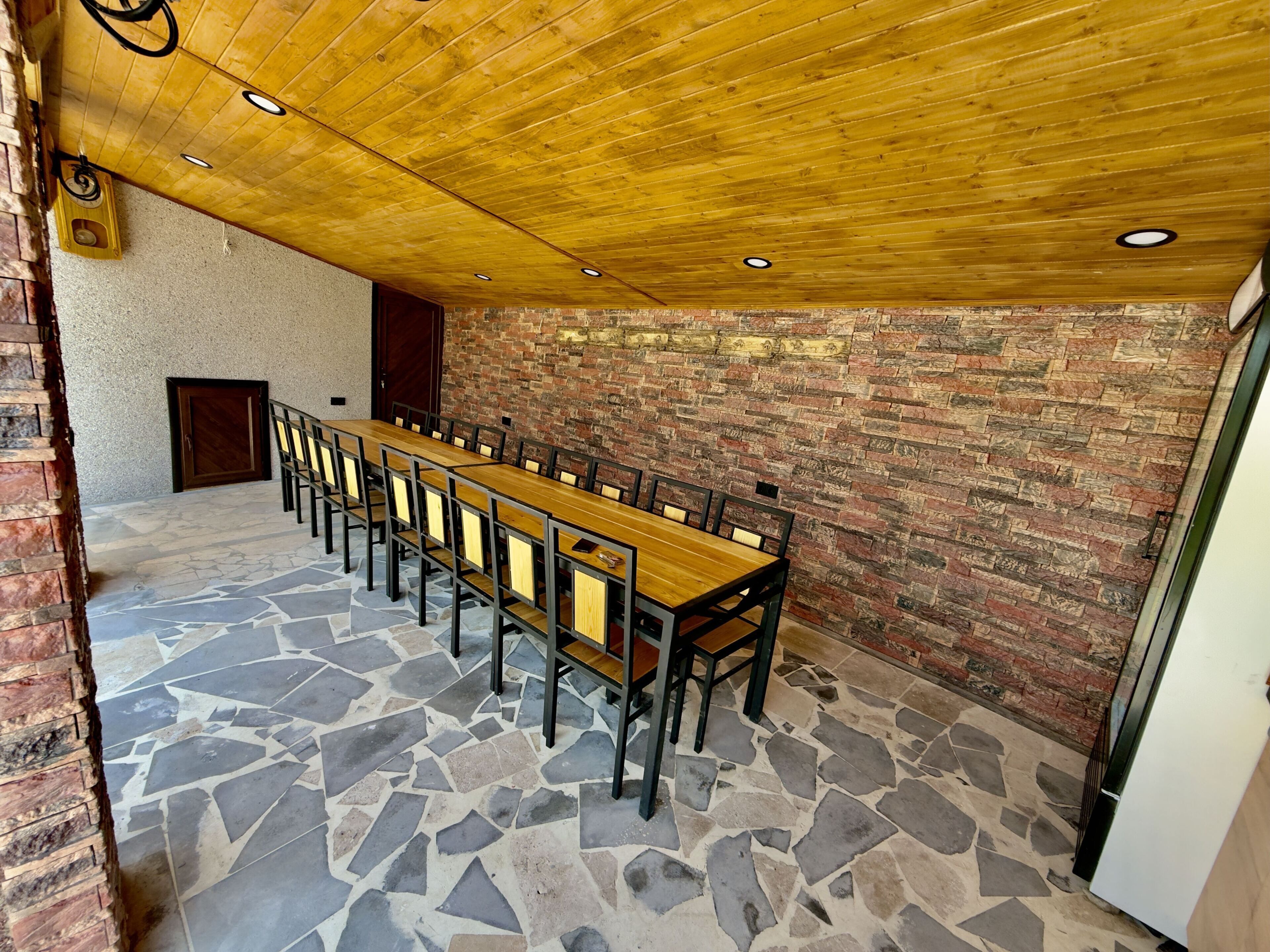 A long wooden table with chairs in a room with a brick wall and a stone floor.