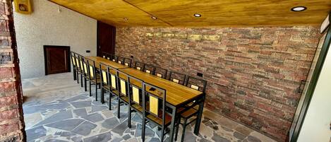 A long wooden table with chairs in a room with a brick wall and a stone floor.