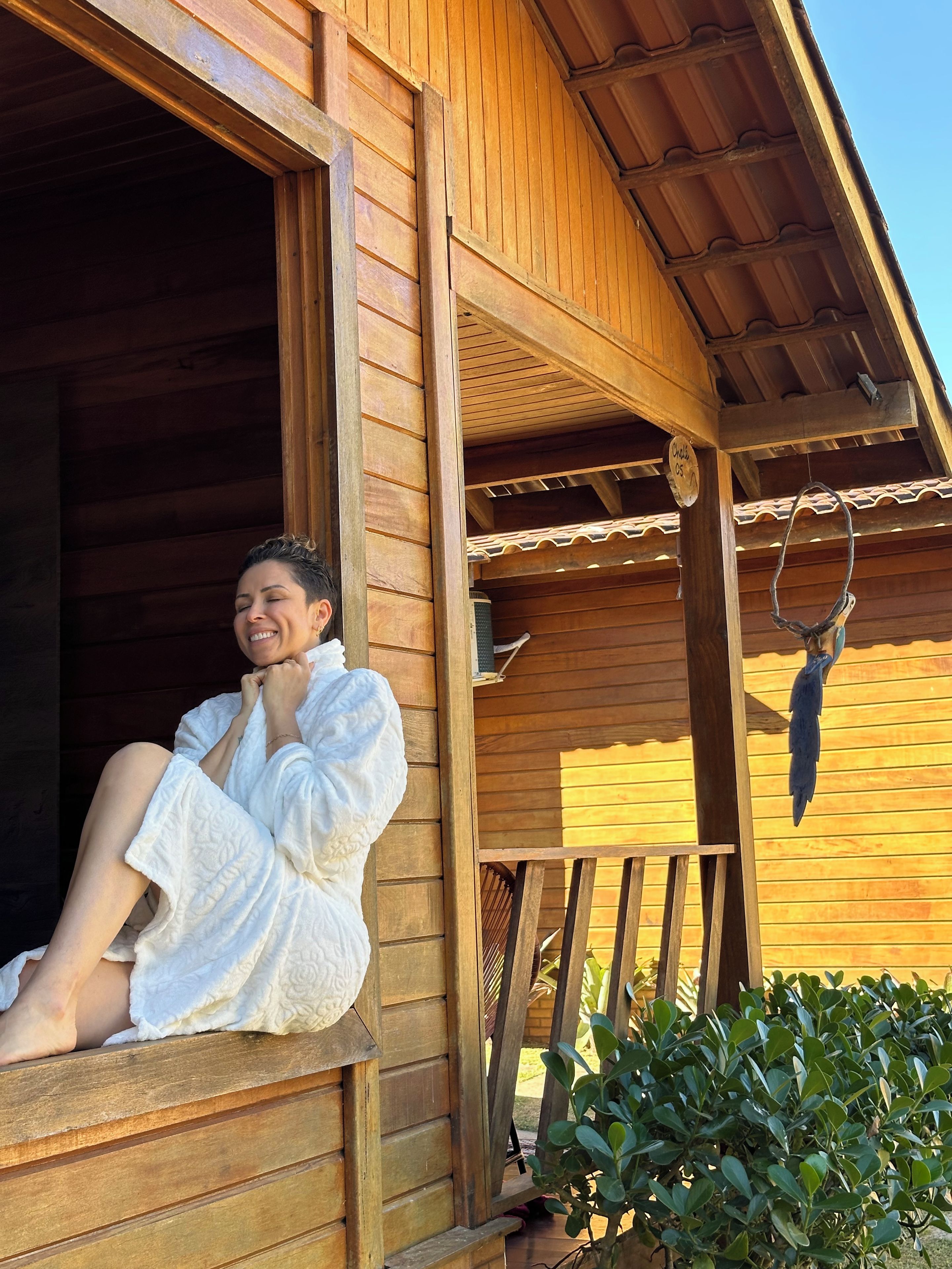 A person sitting on a wooden porch with a wooden railing, wearing a white robe.