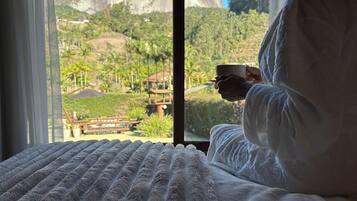 Una persona sentada en una cama con vista a una gran montaña y vegetación.