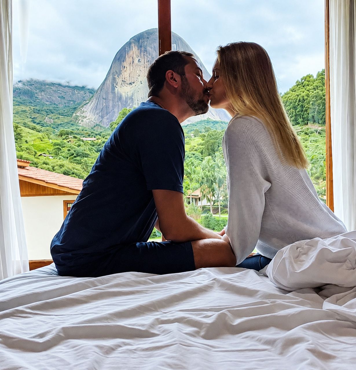 Una pareja sentada en una cama con vistas a un paisaje montañoso.