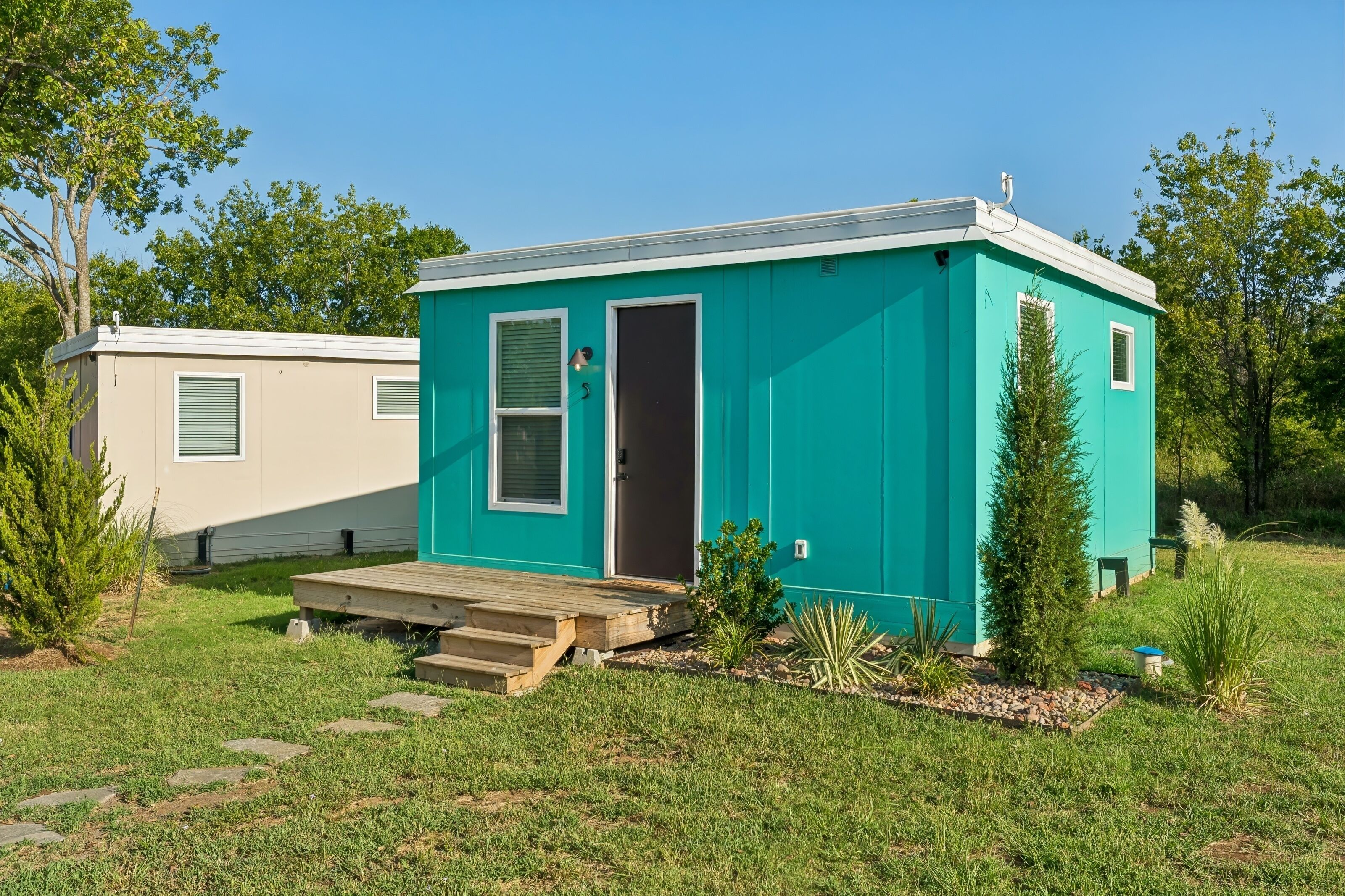 Une petite maison mobile d’un seul étage, de couleur turquoise, avec une porte d’entrée et un petit porche.