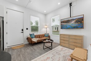 A modern living room with a sofa, a coffee table, a rug, and a painting on the wall. - Modern Boxabl Casita | Stillwater OK | Pasadera 5 (Stillwater)
