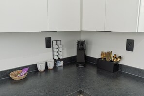 A modern kitchen with white cabinets, a coffee maker, and a utensil holder. - Modern Boxabl Casita | Stillwater OK | Pasadera 5 (Stillwater)