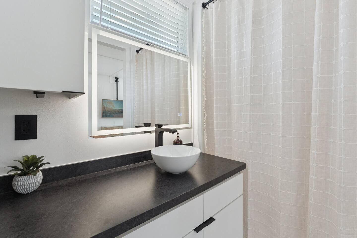 A modern bathroom with a white sink, dark countertop, and a potted plant.