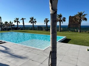 Piscina com vista clara do oceano e uma palmeira ao primeiro plano.