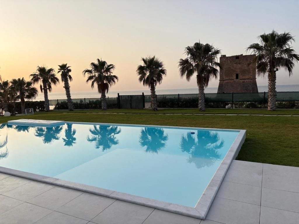 Une piscine offrant une vue dégagée sur la mer, avec un bâtiment historique en arrière-plan.