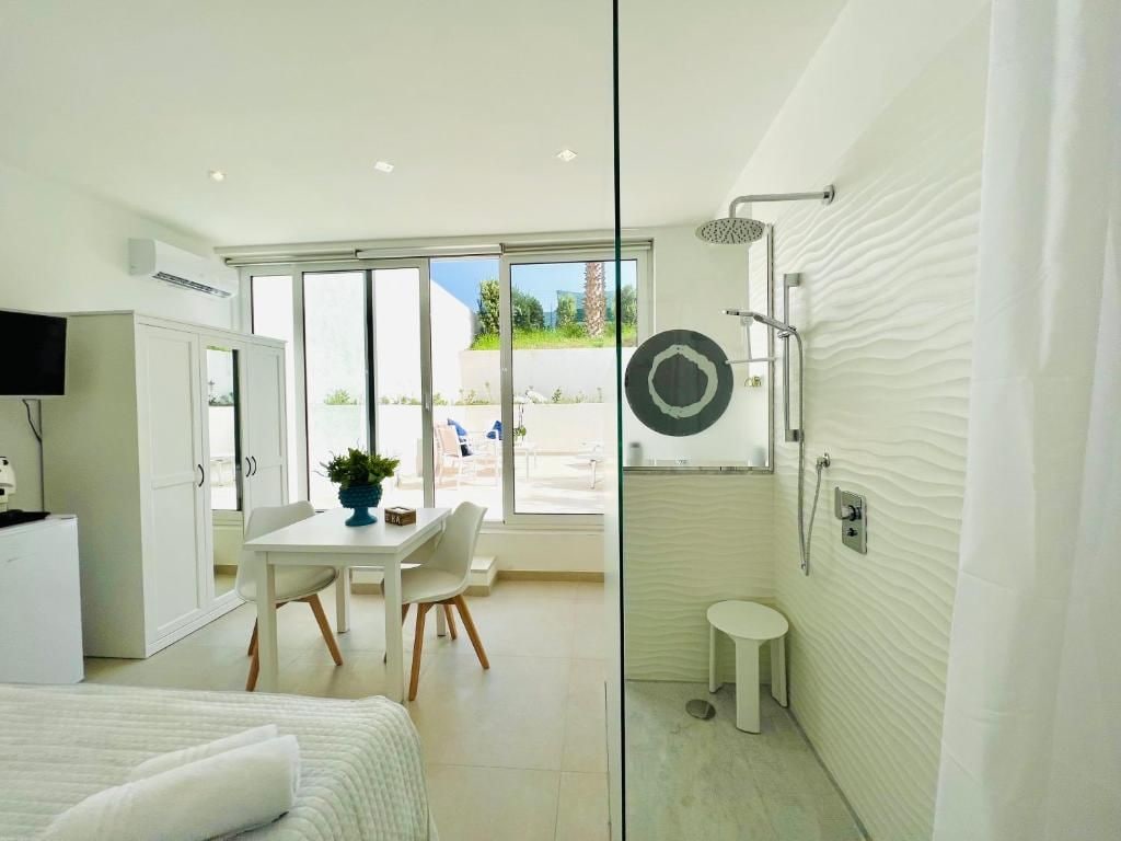 A modern hotel room with a bed, a desk, a chair, a small table, a shower, and a view of the outdoors.
