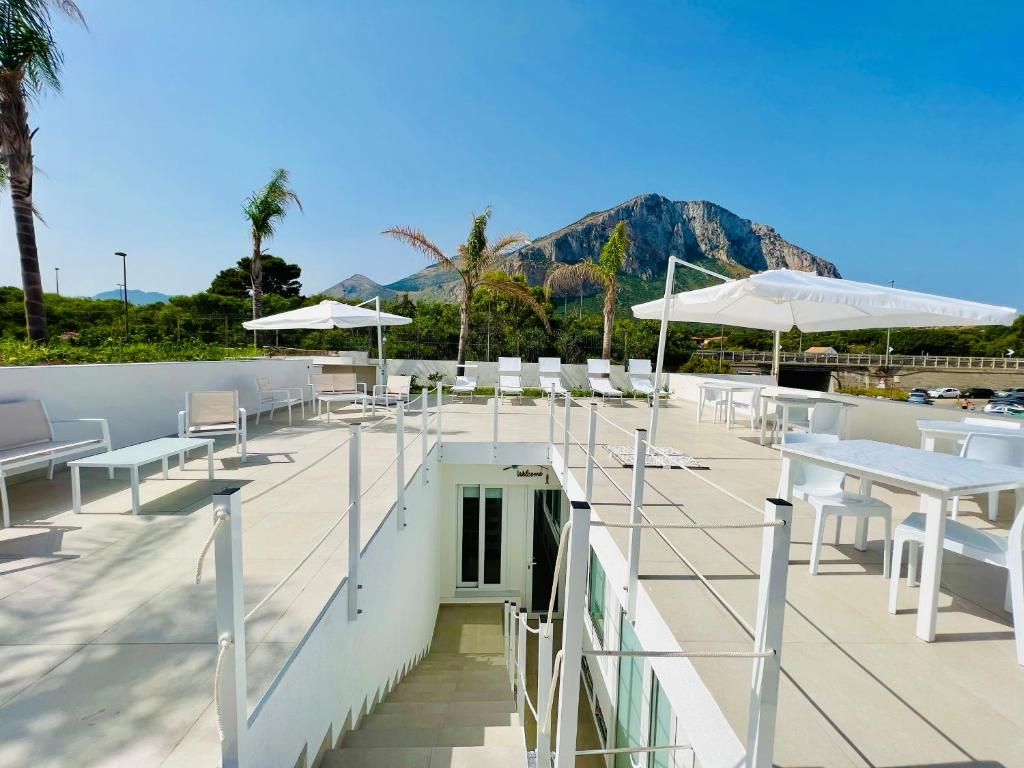Een terras met witte tafels en stoelen, parasols en uitzicht op een berg.