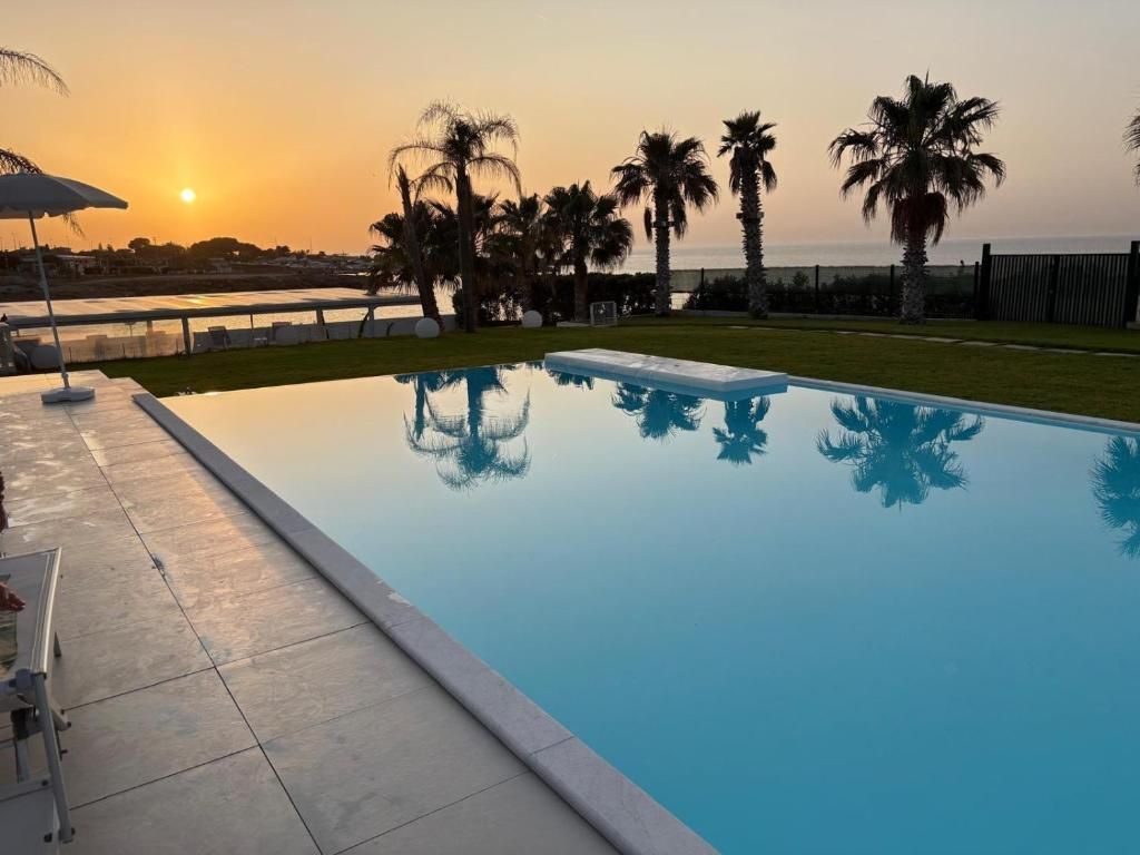 Une piscine offrant une vue dégagée sur le coucher de soleil et les palmiers en arrière-plan.