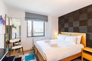 Ein Hotelzimmer mit einem Bett, einem Nachttisch, einem Sessel, einem Schreibtisch, einem Fenster und einer Wand mit strukturierter Wandverkleidung.