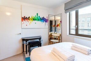 Une chambre d’hôtel comprenant un lit, un bureau, une chaise, un miroir et une fenêtre donnant sur des immeubles.