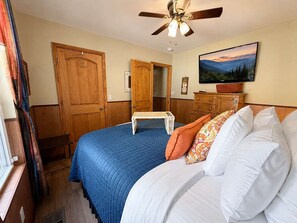 Ein Schlafzimmer mit einem Bett, einem Deckenventilator, einem Fernseher und einem Bild an der Wand.