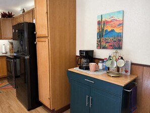 A kitchen with wooden cabinets, a black refrigerator, a coffee maker, and a painting on the wall. - Adorable, easy access, level cabin super clean! (Ruidoso)