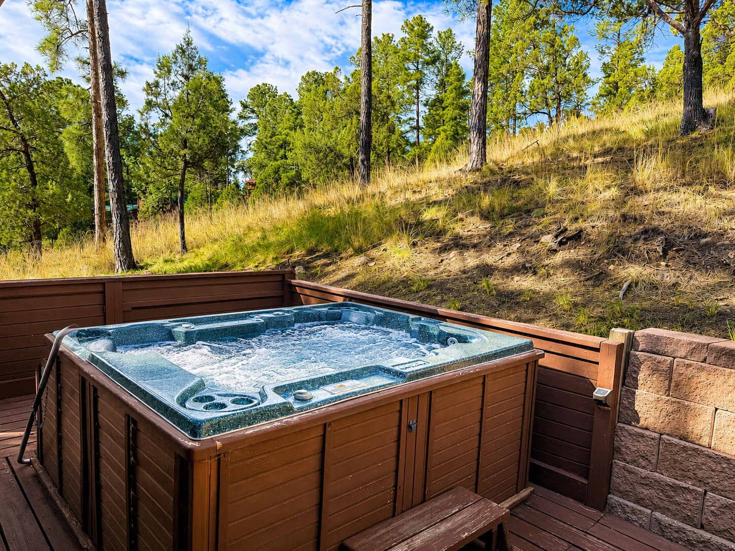 A hot tub on a wooden deck with a view of a grassy hillside and trees.