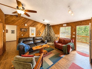 Ein gemütliches Blockhaus-Interieur mit Kamin, Ledersofas, einem Holztisch und einem Deckenventilator.