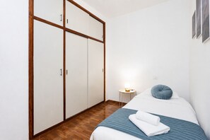 A bedroom with a bed, a bedside table with a lamp, a wardrobe, and a blue pillow. - TenoHomes YSLA Escape Buenavista (Buenavista del Norte)