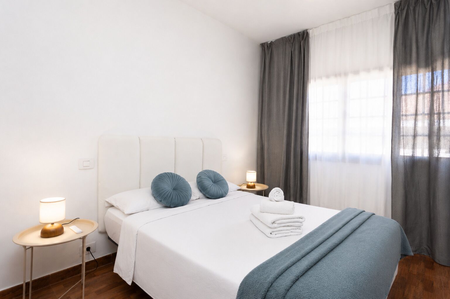 Et hotelværelse med en seng, to sengeborde, lamper og et vindue med gardiner.