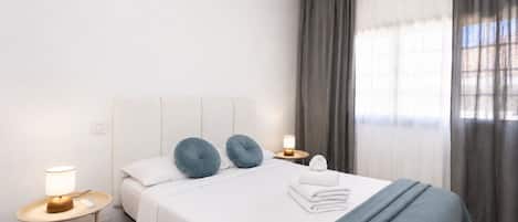 Una habitación de hotel con una cama, dos lámparas de noche, una mesita de noche y un ventanal con cortinas.