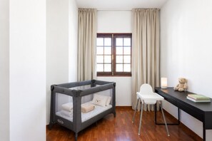 Ein Zimmer mit einem Babybett, einem Schreibtisch, einem Stuhl und einem Fenster mit Vorhängen.