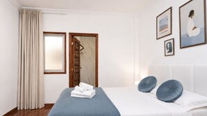 Hotellihuone, jossa on sänky, ikkuna verhoilla, ovi ja seinällä kehystetty taideteos.
