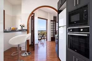 A modern kitchen with a built-in oven and microwave, a bar area with a stool, and a view to a balcony. - TenoHomes YSLA Escape Buenavista (Buenavista del Norte)