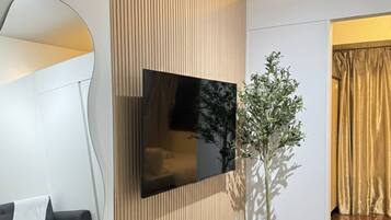 A modern living room with a flat-screen TV mounted on a wooden panel wall, a white console table with decorative items, a black sofa, and a large mirror.