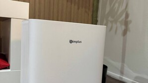 A white Simplus refrigerator in a room with wooden paneling and a shadow of a tree on the wall. - Fully Furnished Makati Condo With Fast Wi-fi and Queen Bed (Makati)